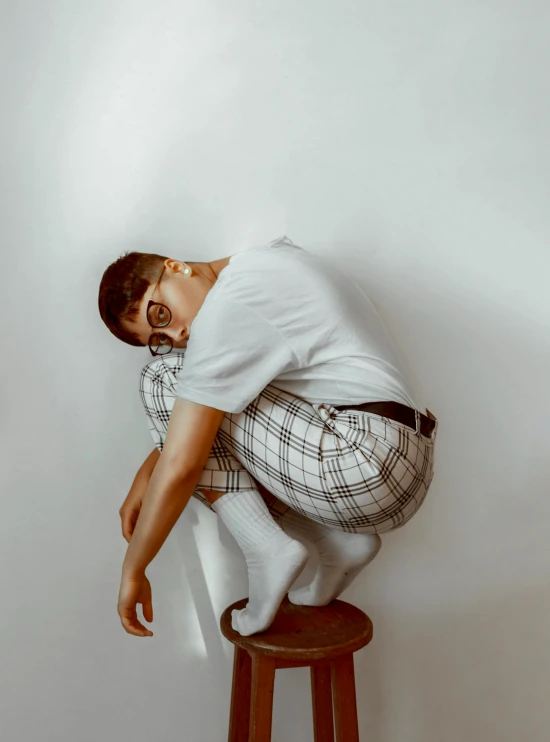 a man sitting on top of a wooden stool, trending on pexels, hyperrealism, wearing pants, checkered floor, bella poarch, hunched over