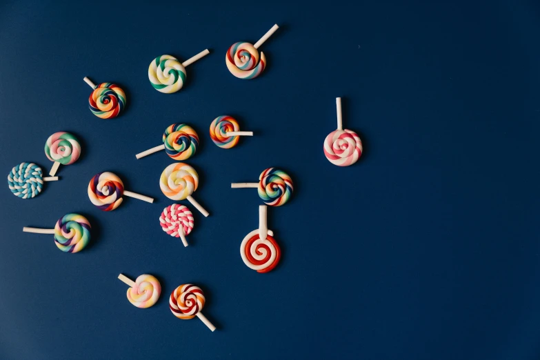 a bunch of lollipops sitting on top of a blue surface, trending on pexels, colorful swirly magical clouds, 1940s food photography, spiral horns!, two - tone