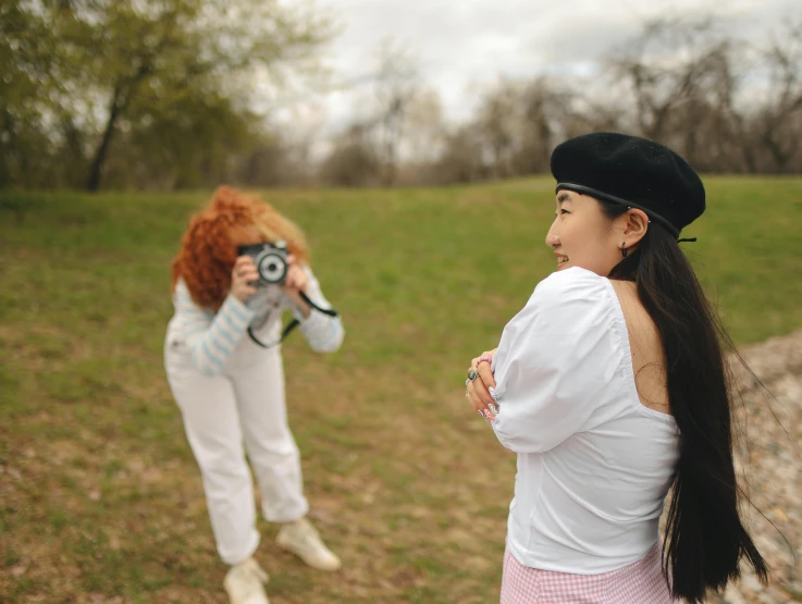 a woman taking a picture of another woman with a camera, trending on pexels, visual art, wearing a french beret, in a open green field, cosplay photo, wearing white clothes