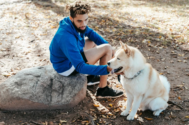 a man sitting on a rock petting a dog, trending on unsplash, wearing a blue hoodie, young man with short, sydney park, federation clothing