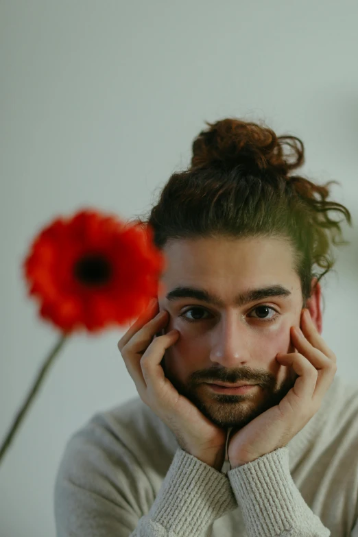 a man sitting in front of a red flower, an album cover, pexels contest winner, antipodeans, hair styled in a bun, headshot profile picture, zac retz, hasan piker