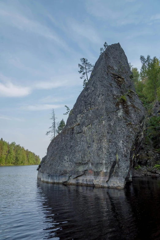 a large rock in the middle of a lake, by Svetlin Velinov, boreal forest, steep cliffs, single file, side