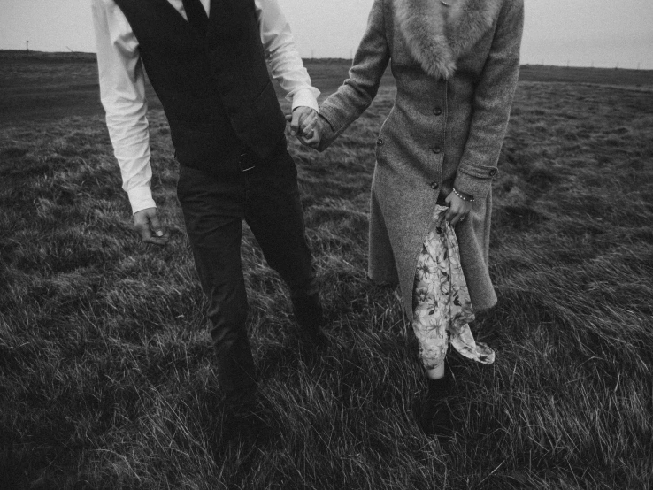 a man and a woman holding hands in a field, a black and white photo, by Emma Andijewska, old wool suit, instagram picture, iceland photography, retro photography