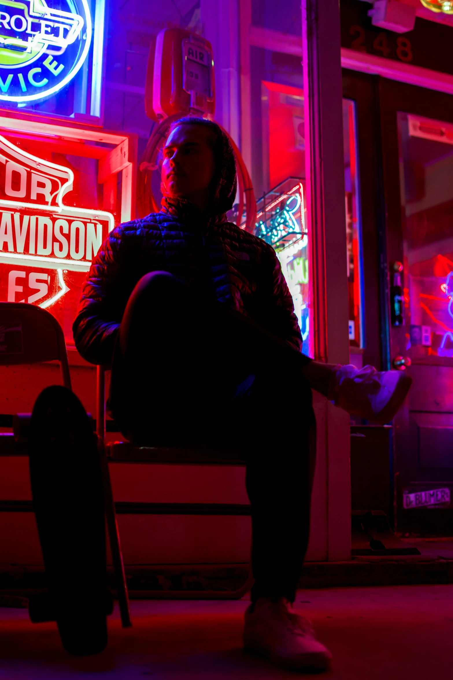 a person sitting on a bench in front of a store, by Matt Cavotta, dramatic neon lighting, frank dillane, red wings, sitting across the room