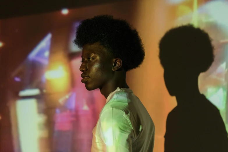 a man standing in front of a projection screen, by Nathalie Rattner, pexels, afrofuturism, black teenage boy, soft light from the side, medium shot of two characters, side profile waist up portrait