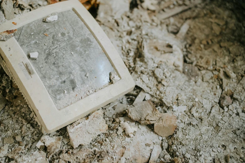 an old computer sitting on top of a pile of rubble, by Emma Andijewska, unsplash, concrete art, background image, recessed, dusty floor, selfie photo