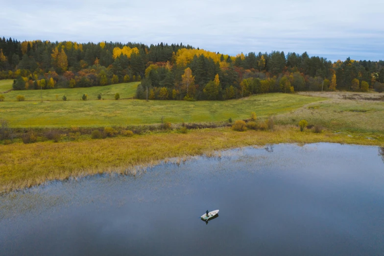 a small boat floating on top of a lake, by Jaakko Mattila, pexels contest winner, land art, autumn field, wide film still, wide high angle view, 3 / 4 wide shot