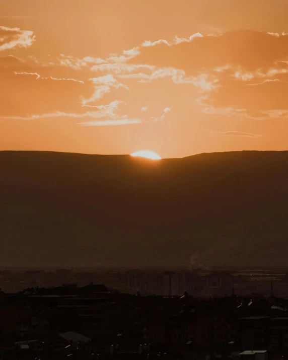 the sun is setting over a city with mountains in the background, pexels contest winner, happening, orange tones, slightly tanned, very accurate photo, sun exploding on the background