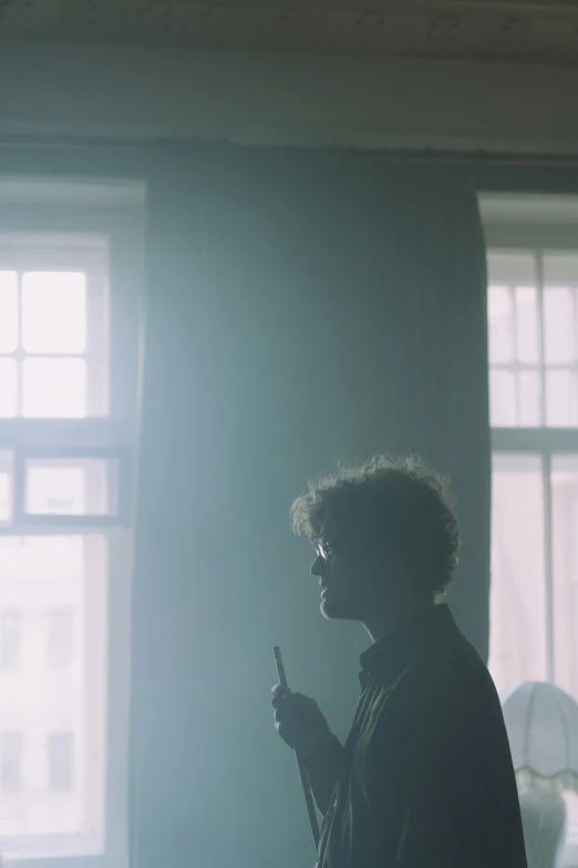 a man that is standing in front of a window, an album cover, pexels, ed sheeran, cinematic backlighting, he is smoking a cigarette, ( ( theatrical ) )