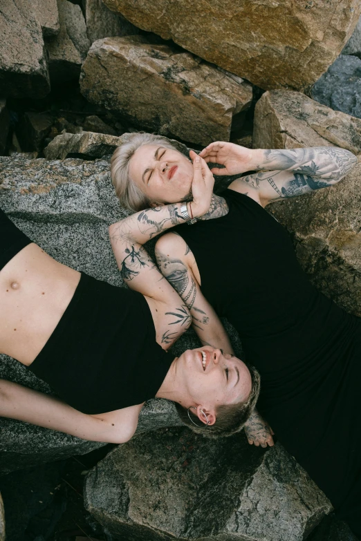 a man and a woman laying on some rocks, a tattoo, inspired by Elsa Bleda, trending on pexels, lesbians, goth aesthetic, beautiful gemini twins, a blond