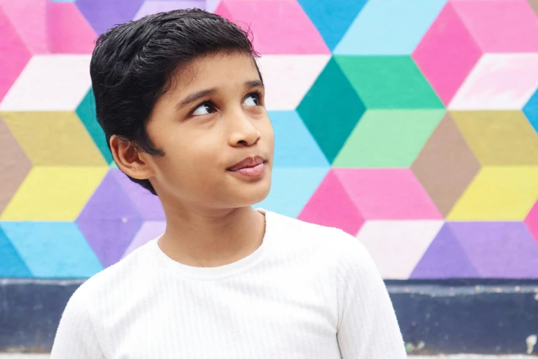 a young boy standing in front of a colorful wall, pexels contest winner, indian girl with brown skin, future coder looking on, androgynous male, boy has short black hair