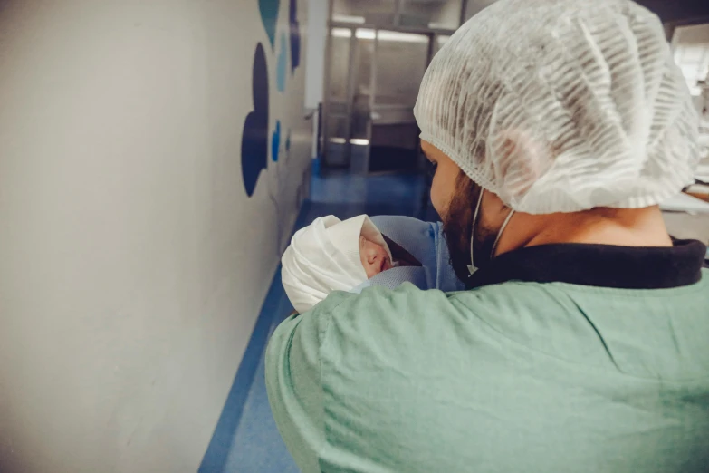 a man holding a baby in a hospital room, by Julia Pishtar, pexels contest winner, happening, face covered, head down, worksafe. instagram photo, surgery theatre