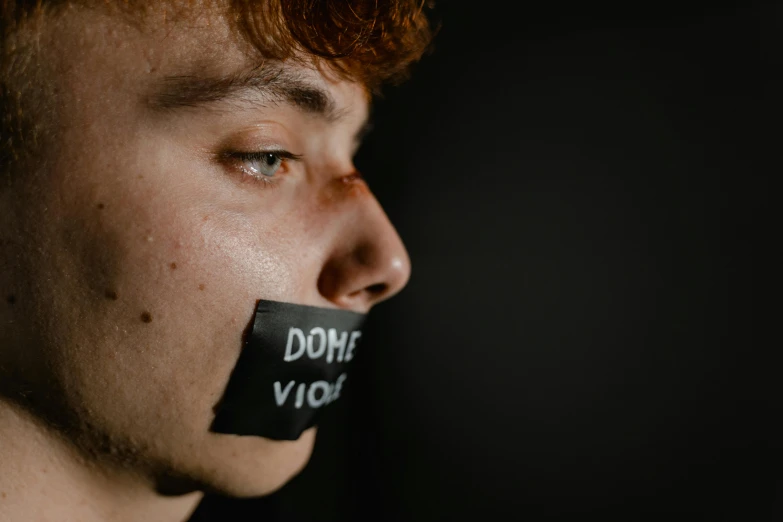 a close up of a person with tape on their mouth, by Robbie Trevino, trending on pexels, subject action: holding sign, joe keery, dominance, silence