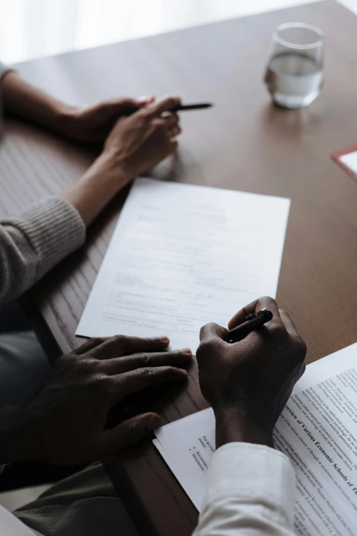 a couple of people sitting at a table with papers, reaching out to each other, black man, pen and paper, premium quality