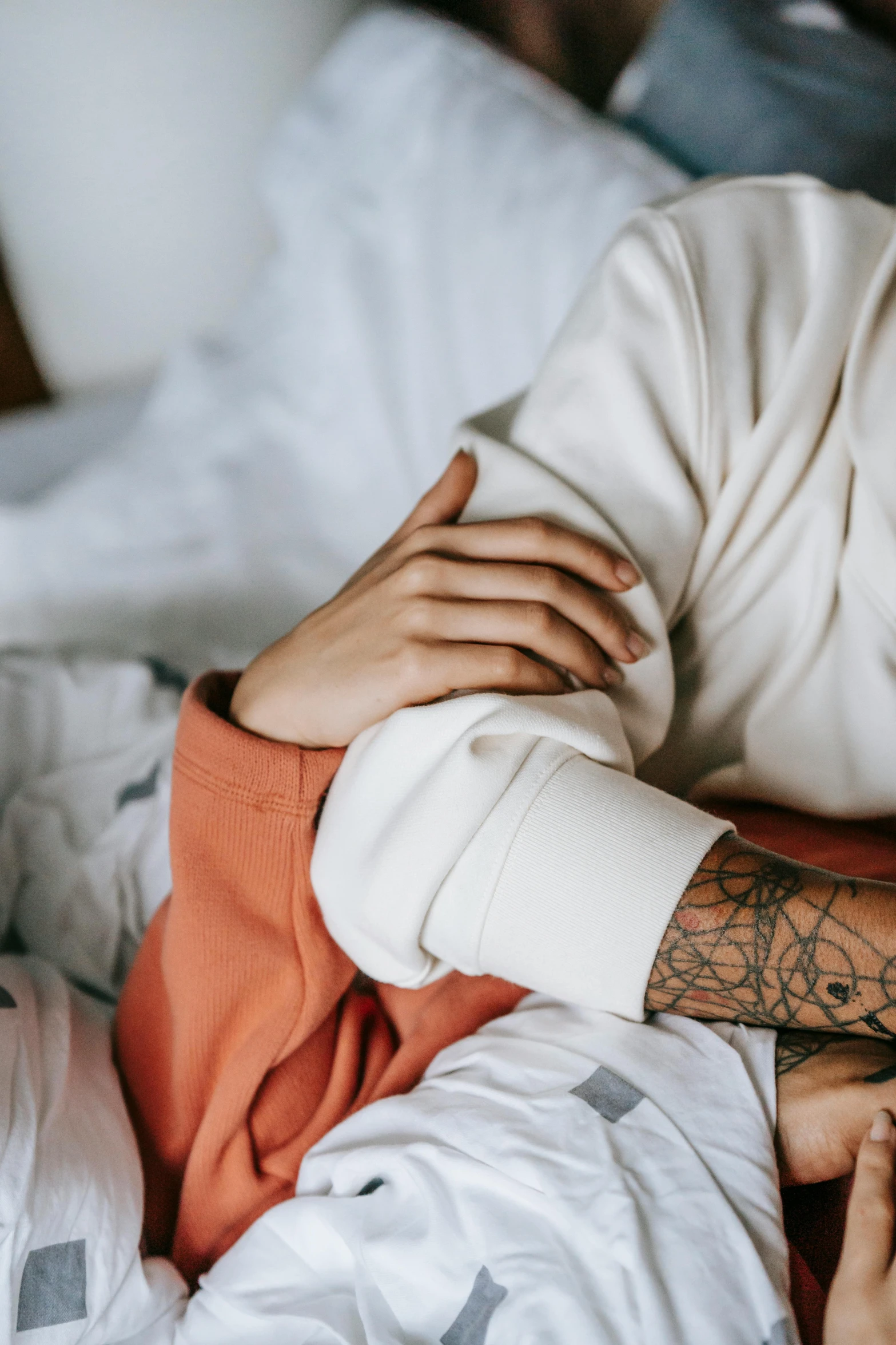 a man laying on top of a bed next to a woman, a tattoo, inspired by Elsa Bleda, trending on pexels, white sleeves, insectile forearms folded, warm and soft and subdued colors, closeup of arms