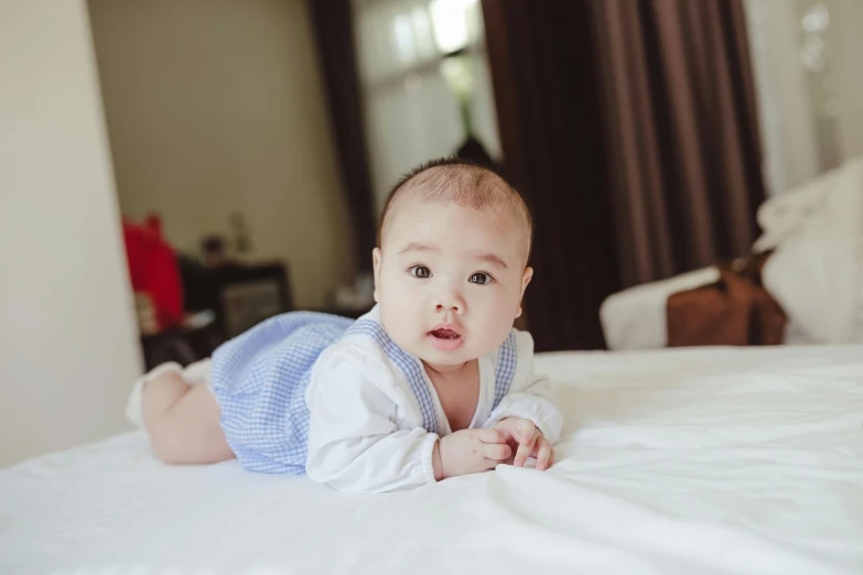 a baby laying on top of a white bed, inspired by Li Shixing, pexels contest winner, happening, well - dressed, asian male, blue, highly polished