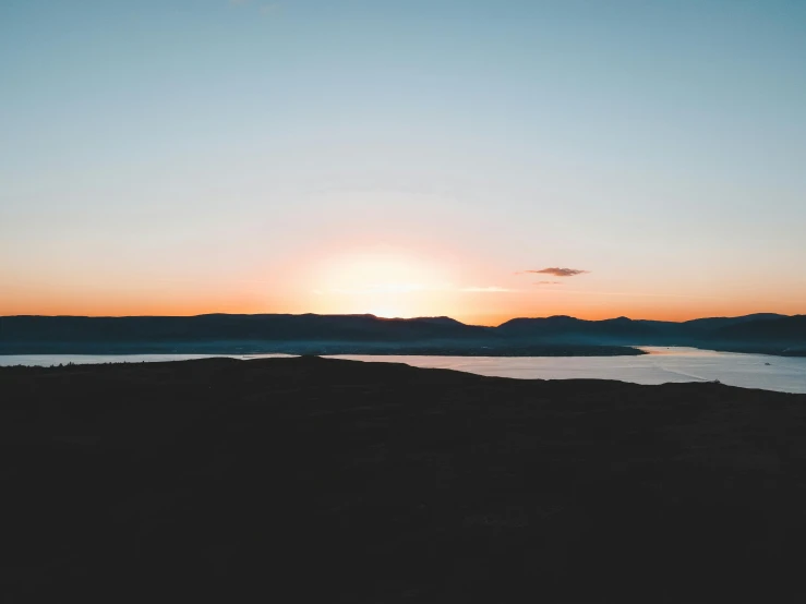 the sun is setting over a body of water, pexels contest winner, black mountains, sparse mountains on the horizon, wide high angle view, orkney islands