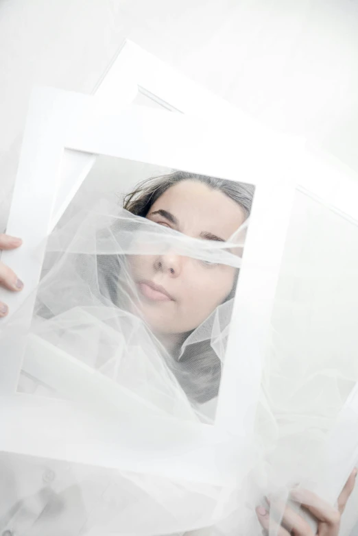 a close up of a person holding a sheet of paper, an album cover, inspired by Anna Füssli, pexels contest winner, plasticien, white transparent veil, sterile, face photo, hiding