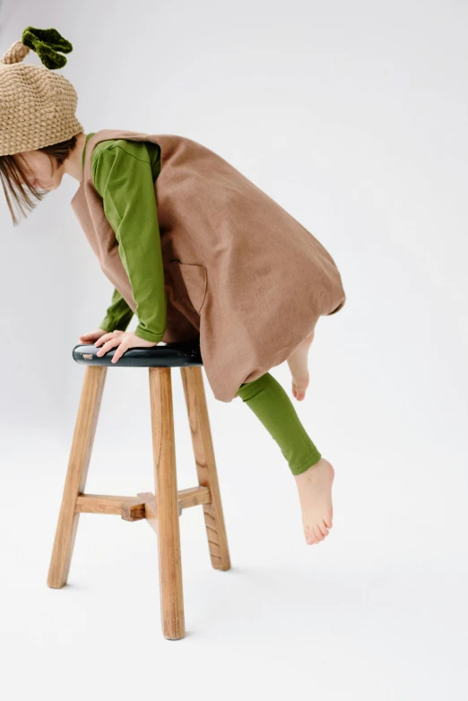 a little girl that is sitting on a stool, by Ai-Mitsu, unsplash, green and brown clothes, like a catalog photograph, bent - over posture, for kids