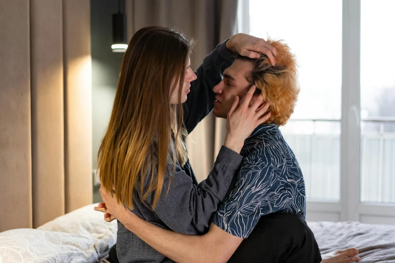 a woman sitting on top of a bed next to a man, by Julia Pishtar, trending on pexels, romanticism, lesbian embrace, touching heads, pale skin curly blond hair, brunette boy and redhead boy