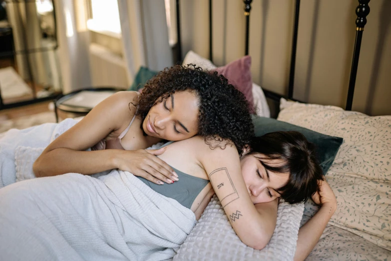 a couple of women laying on top of a bed, trending on pexels, arm around her neck, queer woman, realistic », comforting and familiar