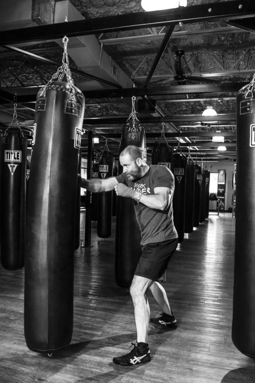 a man hitting a punching bag in a gym, a black and white photo, by Dave Melvin, jason statham, uploaded, 30 year old man :: athletic, robb cobb