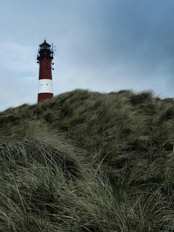 a red and white lighthouse sitting on top of a grass covered hill, by Eglon van der Neer, unsplash, modernism, hasselblad photo, cold stormy wind, 🚿🗝📝, square