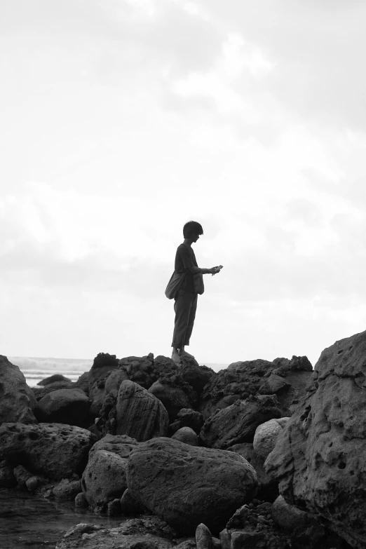 a black and white photo of a person standing on rocks, inspired by Sergio Larraín, shabab alizadeh, alternate album cover, ( ( ( kauai ) ) ), musician