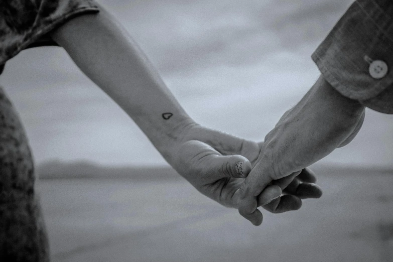 a black and white photo of two people holding hands, trending on pexels, photograph of a sleeve tattoo, desaturated, uploaded, colored photo
