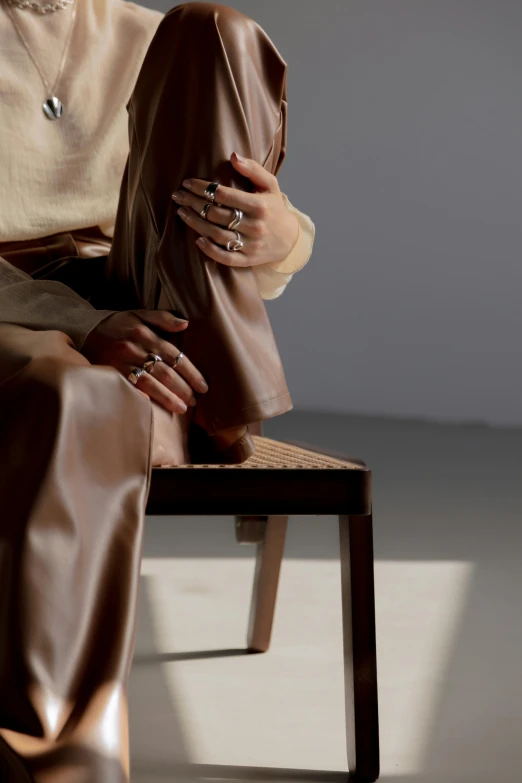 a woman sitting on top of a wooden chair, trending on unsplash, photorealism, wearing two metallic rings, wearing brown robes, margiela campaign, leathery