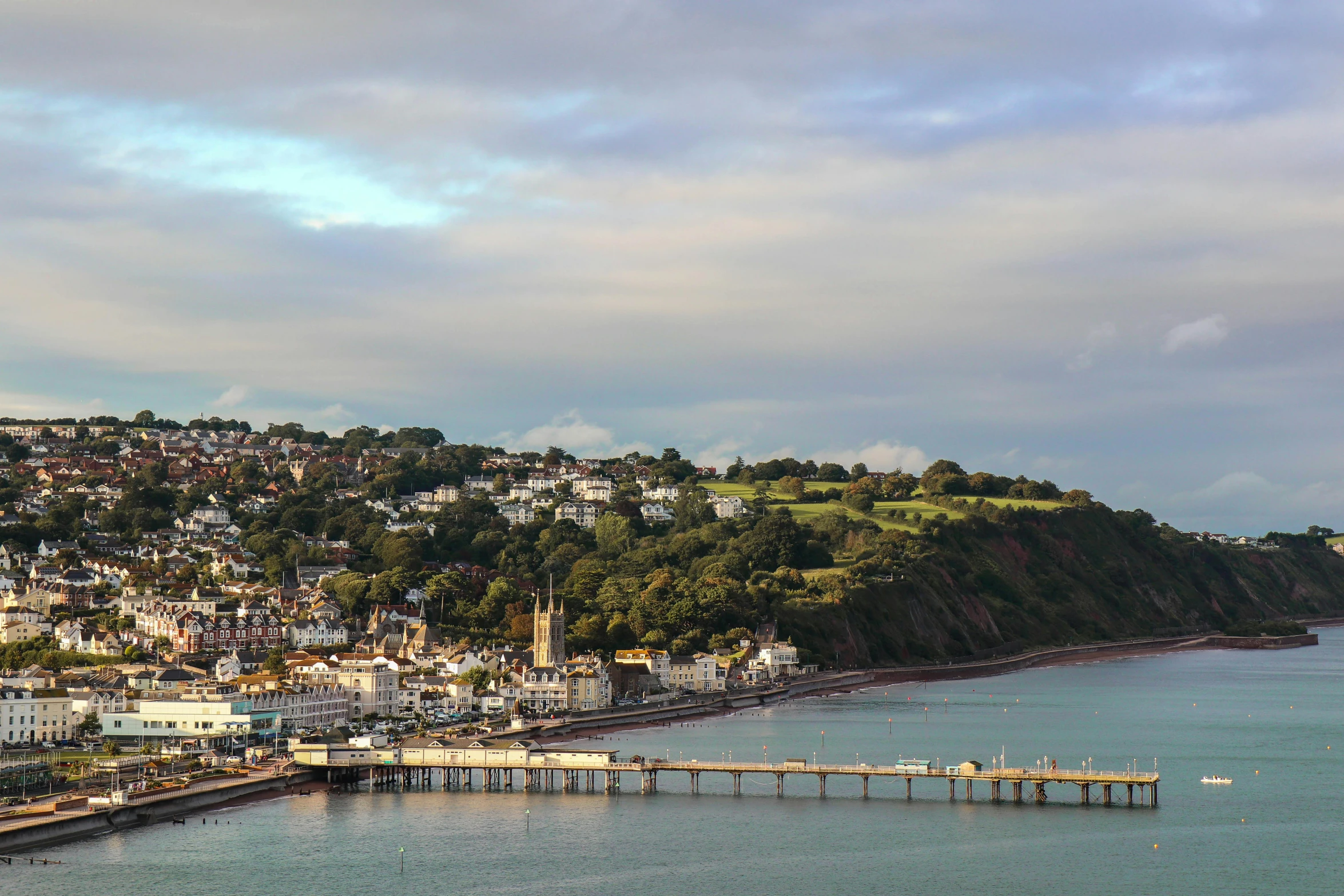 a large body of water next to a lush green hillside, by Rachel Reckitt, pexels contest winner, renaissance, wood pier and houses, seaview, evening light, upon a peak in darien