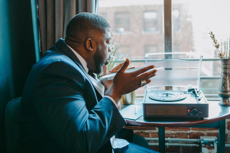 a man in a suit sitting at a table with a record player, pexels contest winner, looking out the window, thicc, instagram post, corporate memphis