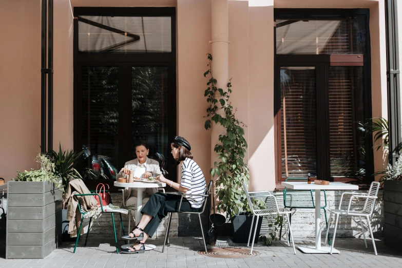 a couple of people that are sitting at a table, by Lee Loughridge, pexels contest winner, plants and patio, aussie baristas, pastel hues, tall terrace