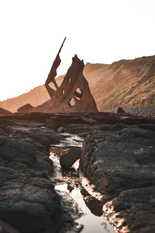 a man standing on top of a rock next to a river, an abstract sculpture, by David Donaldson, unsplash contest winner, land art, gothic ship on ocean, charred, on beach, marsden