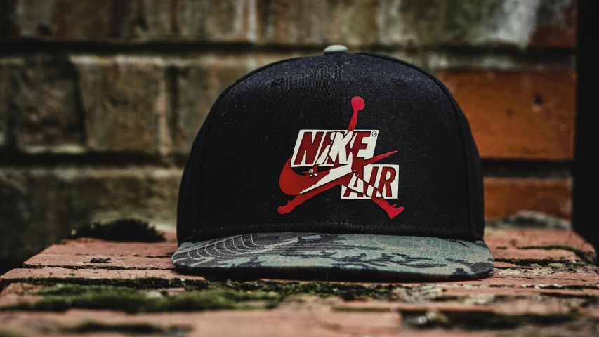 a baseball cap sitting on top of a brick wall, a cartoon, by Niels Lergaard, pexels contest winner, graffiti, “air jordan 1, camo, black and red, large nike logo