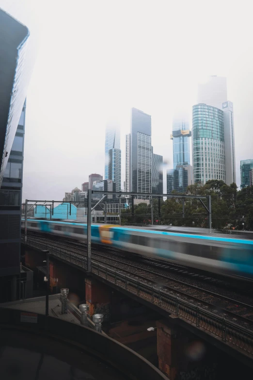 a train traveling through a city next to tall buildings, melbourne, misty weather, stacked image, fan favorite