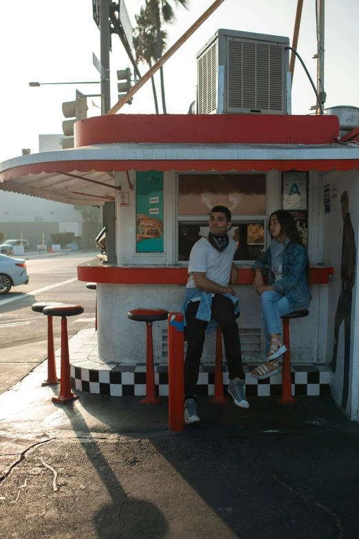 a couple of people that are sitting on a bench, standing in a parking lot, diner scene, sitting on top a table, at the counter