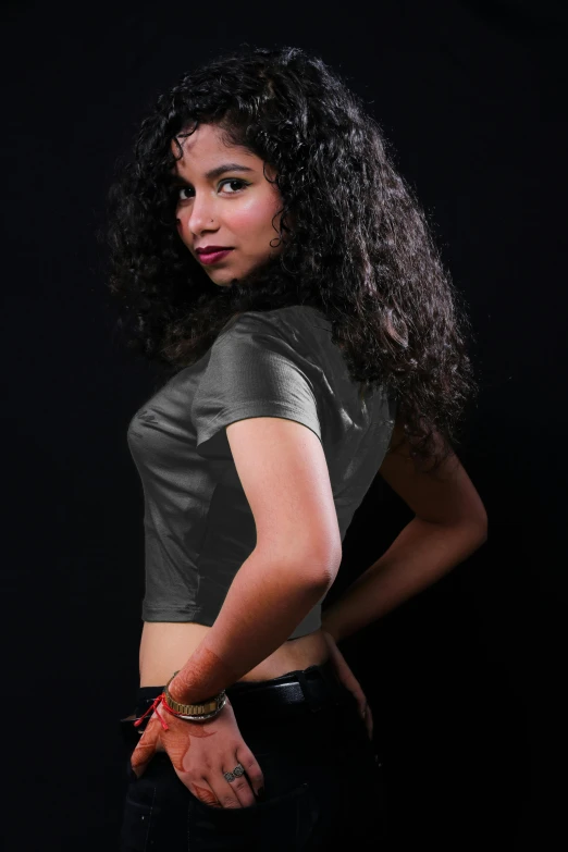 a woman standing with her hands on her hips, an album cover, by reyna rochin, pexels contest winner, (dark shorter curly hair), indian super model, wearing a black t-shirt, grey skin