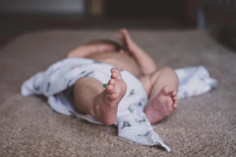 a baby laying on its back on the floor, by Will Ellis, pexels contest winner, happening, bare foot, high resolution, covered with blanket, thighs close up