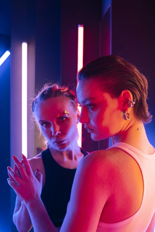 a couple of women standing in front of a mirror, a portrait, inspired by Nan Goldin, trending on pexels, lasers and neon circuits, very sweaty, hybrid of gal gadot, intricate led jewellery