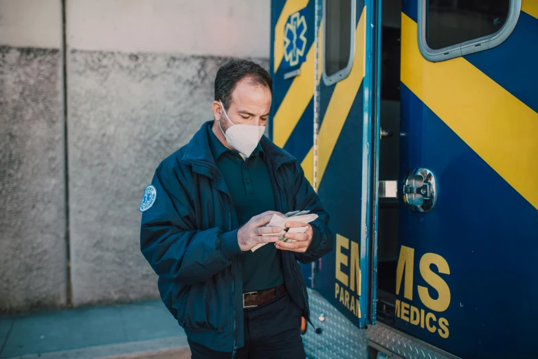 a man wearing a face mask standing in front of a train, by Meredith Dillman, pexels, ambulance, he is holding a smartphone, navy, profile image