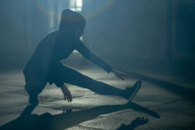 a person on a skateboard in a dark room, pexels contest winner, doing splits and stretching, in a hoodie, early morning light, grey mist