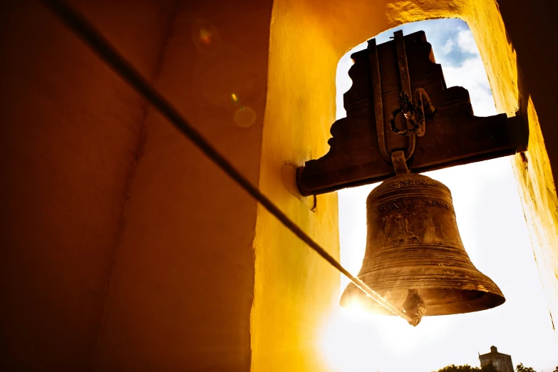 a bell hanging from the side of a building, by Matthias Stom, unsplash, radiating golden light, sri lanka, tlaquepaque, ad image