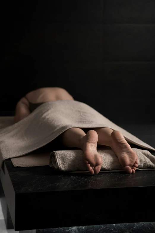 a person laying on top of a bed covered in a blanket, inspired by Robert Mapplethorpe, unsplash, hyperrealism, spa, dark and beige atmosphere, wearing a towel, on display