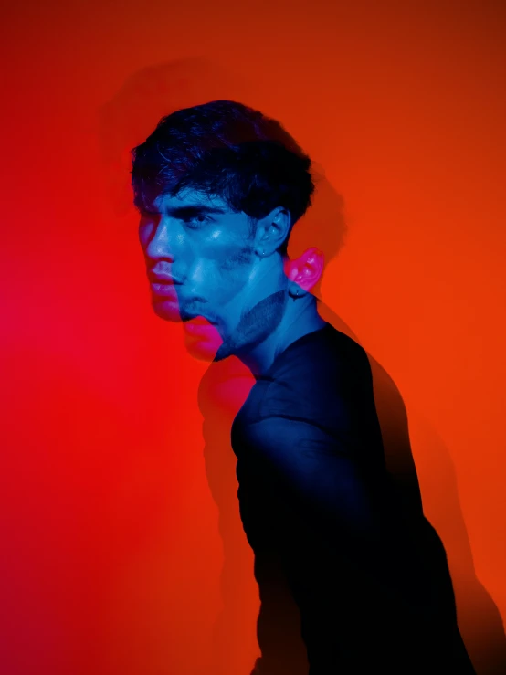 a man standing in front of a red wall, an album cover, by Alexis Grimou, pexels contest winner, neo-fauvism, with high cheekbones, orange and blue tones, blacklight reacting, color splash