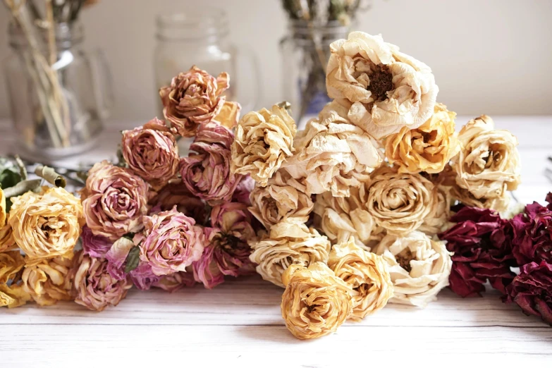 a bunch of dried flowers on a table, large rose flower head, gold flaked flowers, hand - tinted, rose tones