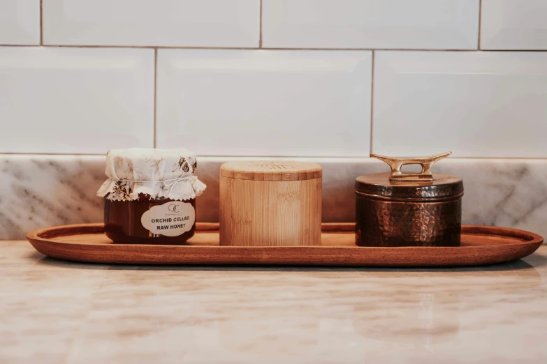 two jars of honey sit on a tray on a counter, inspired by Kanō Shōsenin, brown, skincare, wooden banks, medium