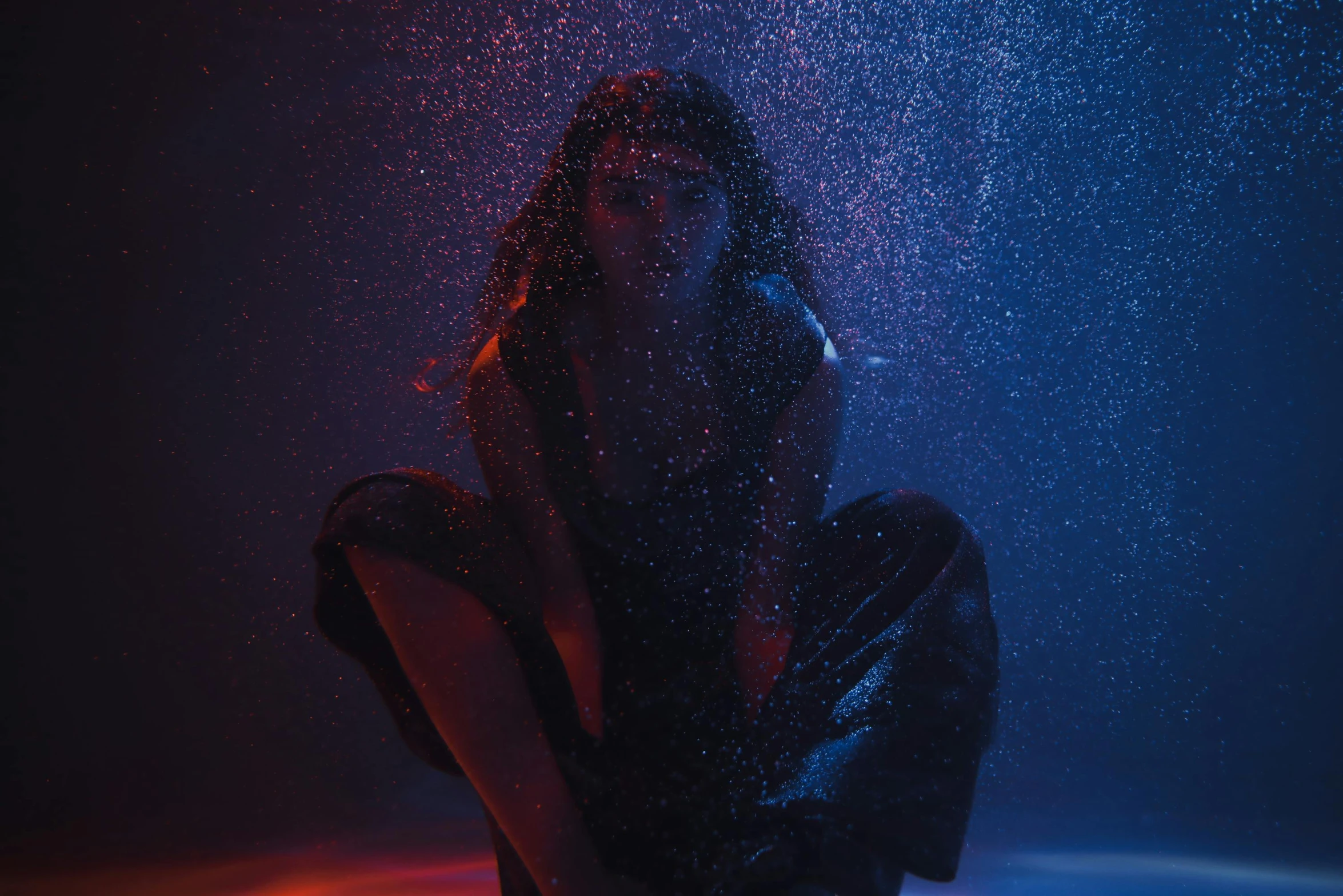 a woman sitting on the ground in the rain, an album cover, unsplash contest winner, holography, red and blue black light, water particles, madison beer as leeloo, dark. studio lighting