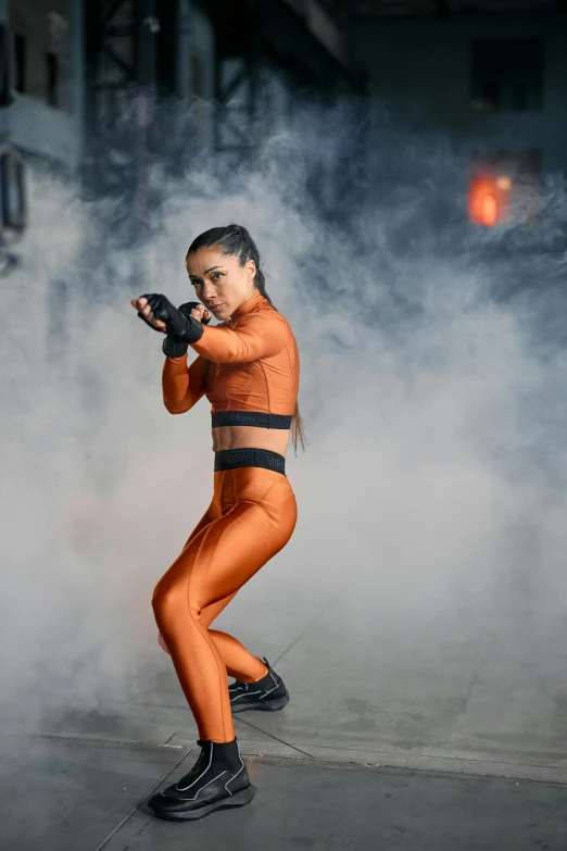 a woman in an orange outfit holding a gun, pexels contest winner, happening, heroic muay thai stance pose, olivia culpo, wearing techwear and armor, live performance