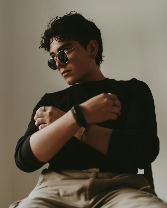 a man sitting on a chair with his arms crossed, an album cover, inspired by Ion Andreescu, trending on pexels, sumatraism, lgbt, wearing shades, androgyny, profile image